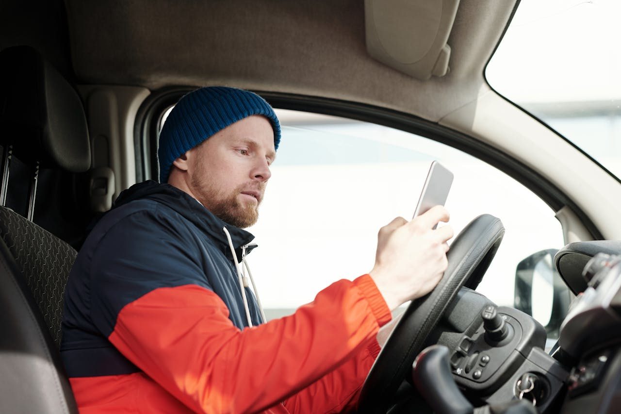 Postdienstleister im Auto Mann im Auto, hält ein Smartphone und sitzt am Steuer.