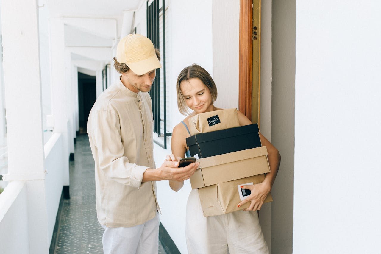 Paketübergabe an Kunde Mann zeigt Frau auf Handy, während sie Pakete vor einer Wohnungstür halten.