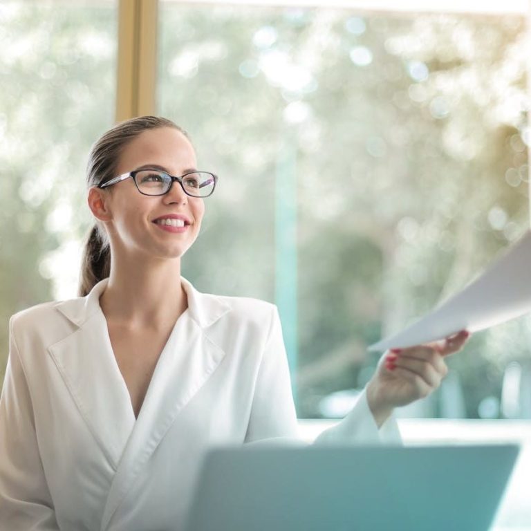 Frau in Büro Frau in weisser Bluse mit Brille, lächelt, hält Unterlagen, in einem modernen Büro.