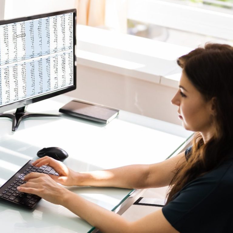 Frau am Computer Frau arbeitet an einem Schreibtisch mit Computer und Tastatur, Daten auf dem Monitor.